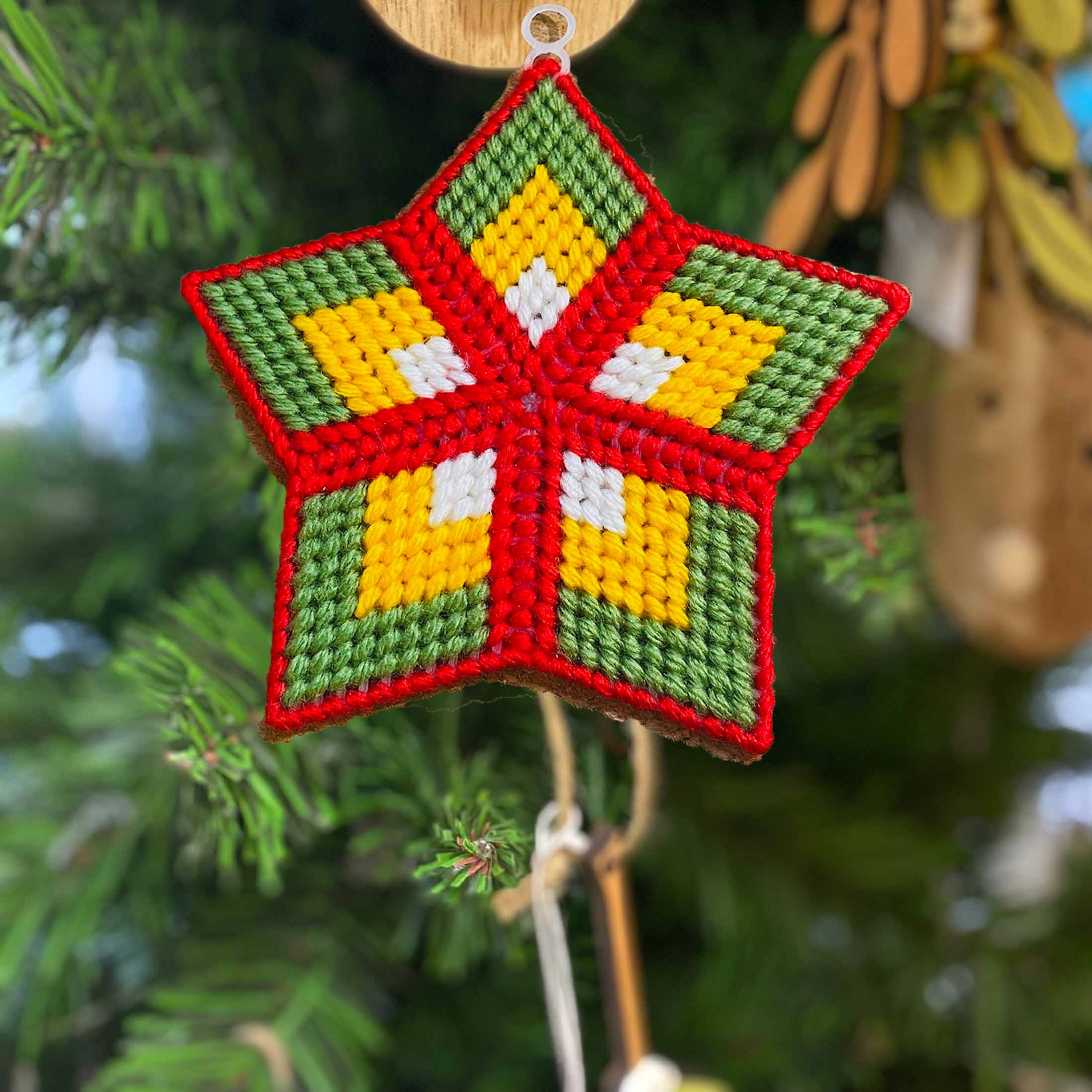 A colourful star made of stitched threads in front of a Christmas tree.
