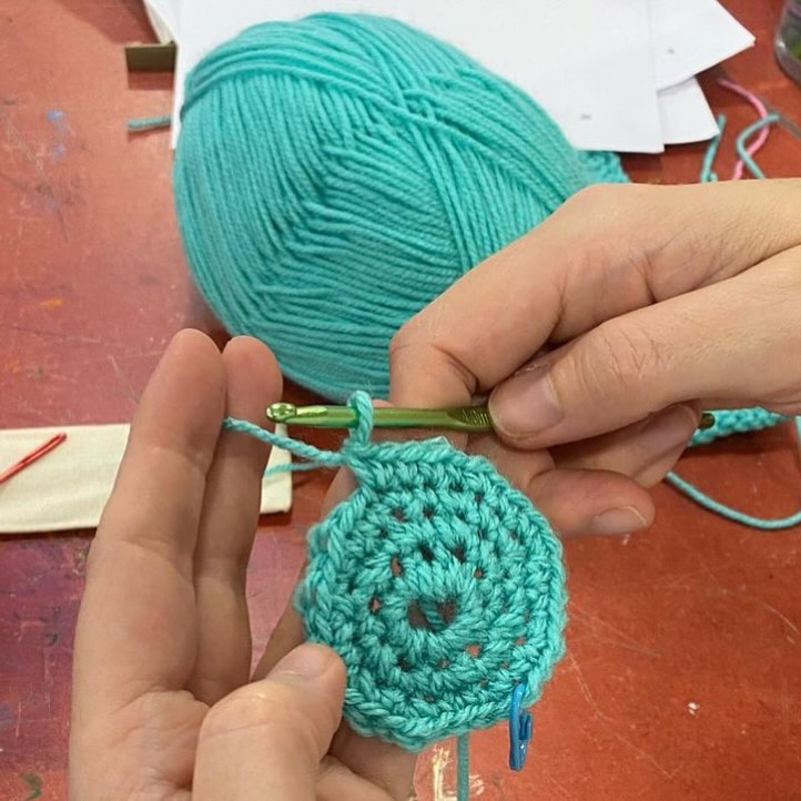 A hand crocheting a circle out of teal yarn.