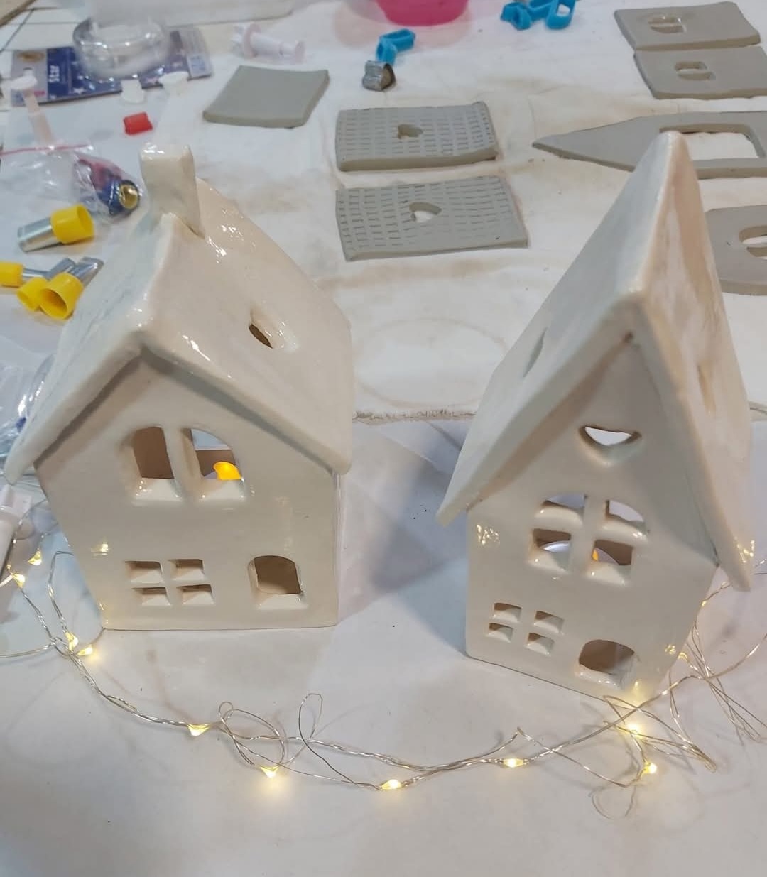Two cream ceramic houses with a string of lights in front of them.