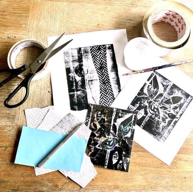 Paper, scissors, tape and paint brushes are scattered about with inked paper.