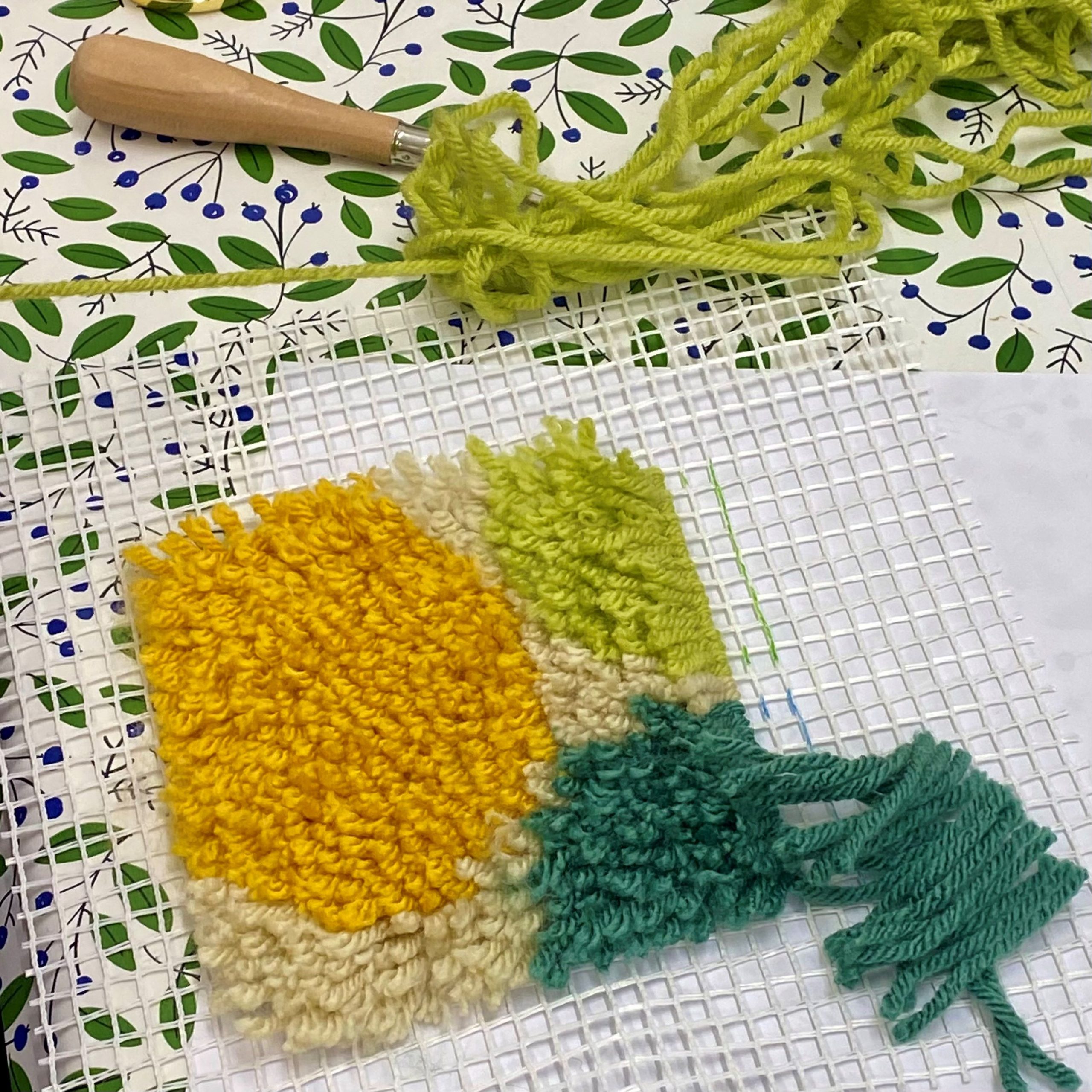 A tiled piece with yellow and green yarns punch through the holes.