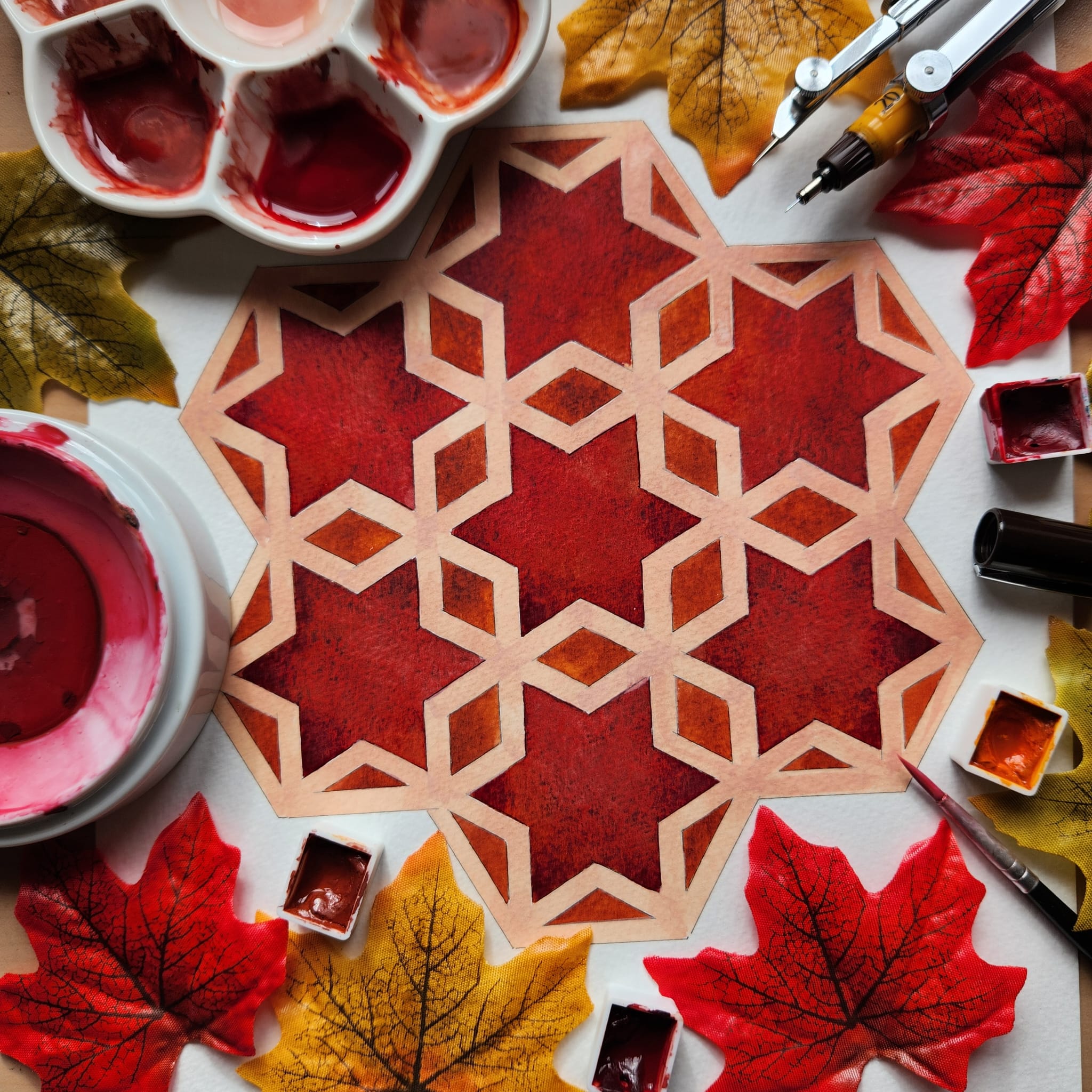 A red Islamic pattern surrounded by red and yellow leaves.