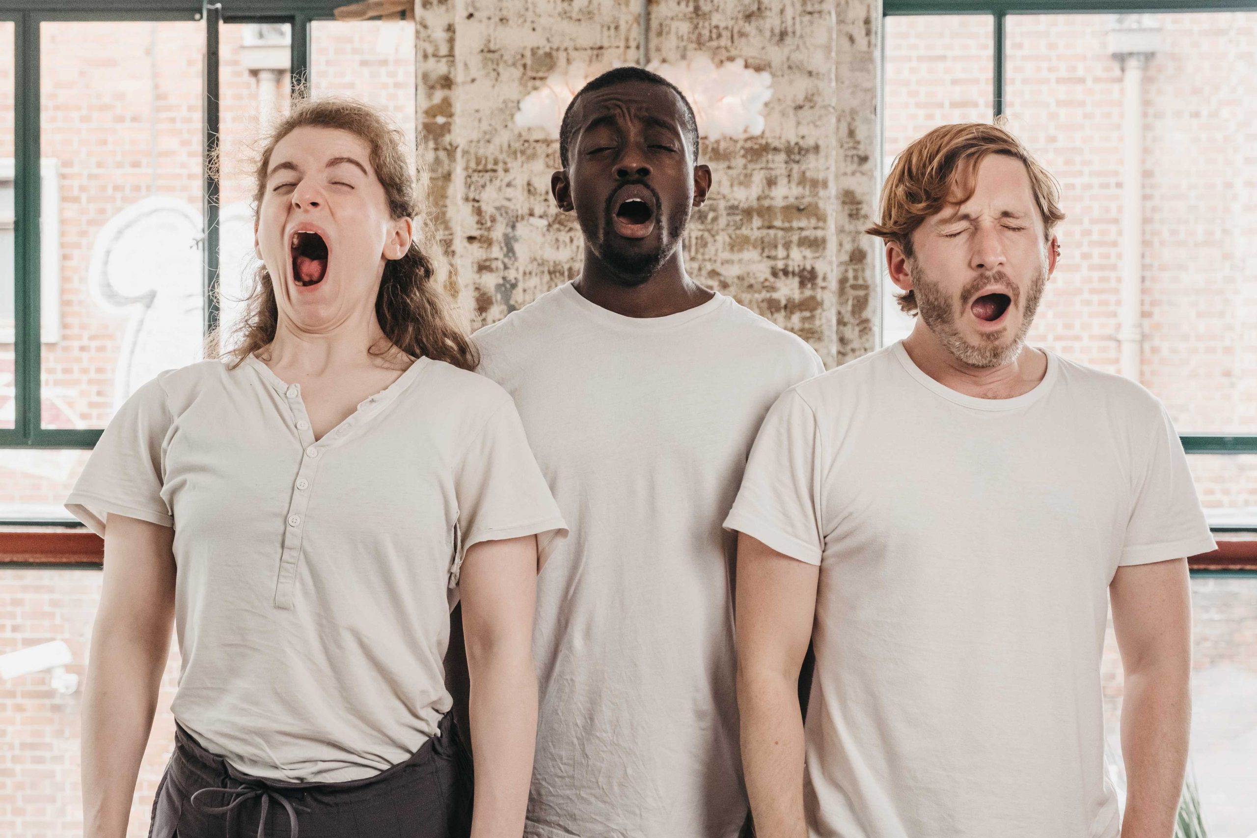 A white women, a black man and a white man all wearing white shirts and yawning together.