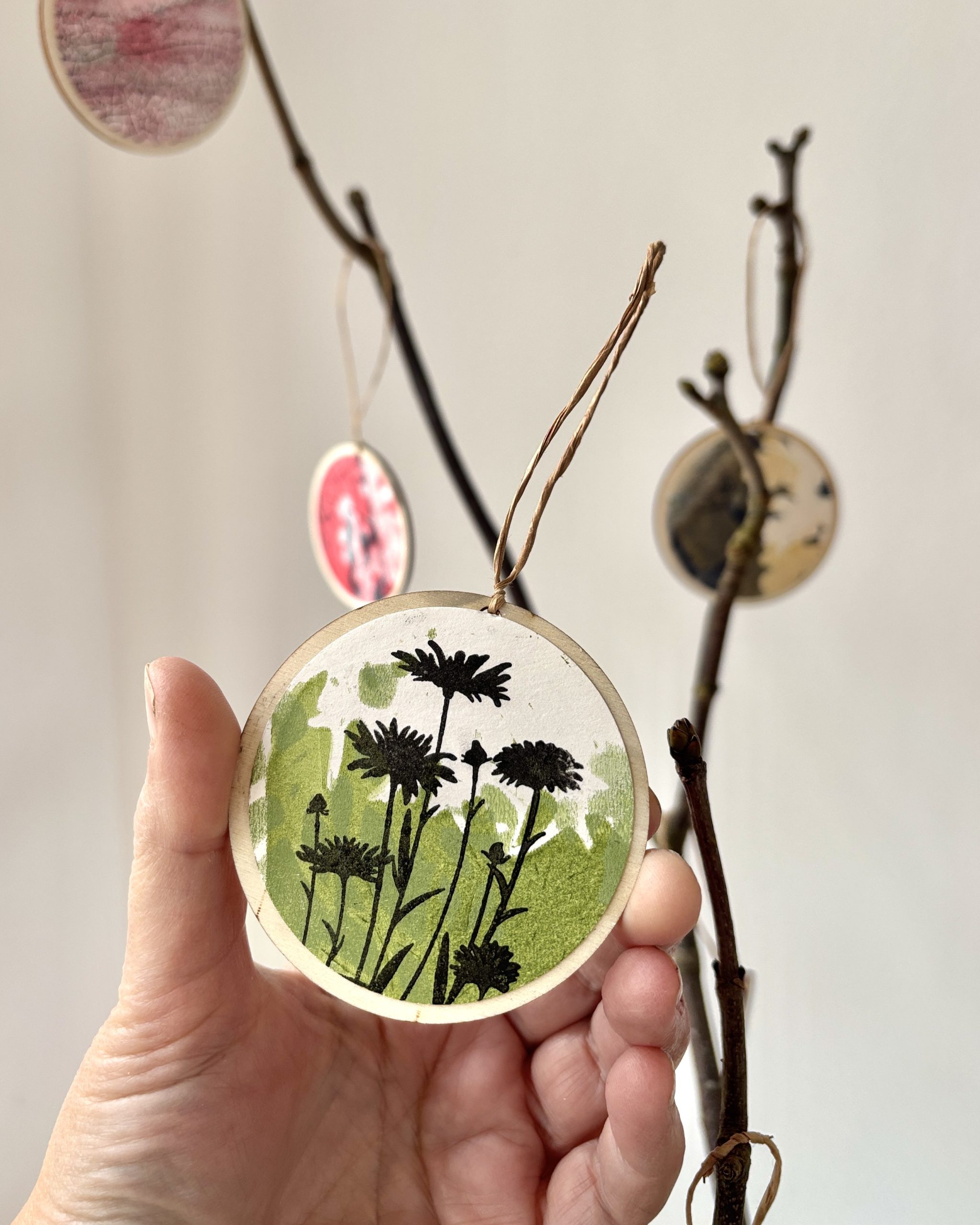 A hand holding up a wooden circle with botanic's painted onto its surface.