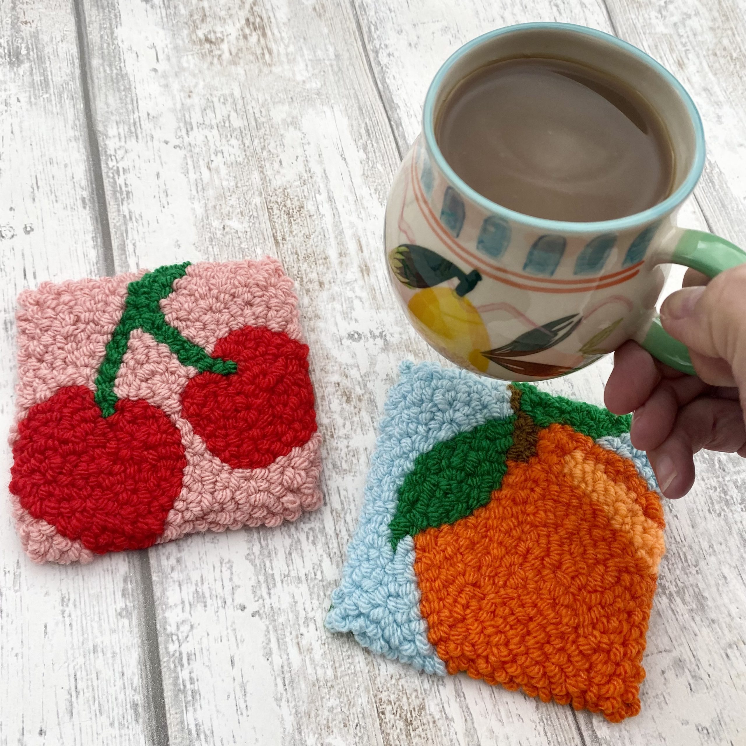 A punch needle coaster of a cherry and a peach.