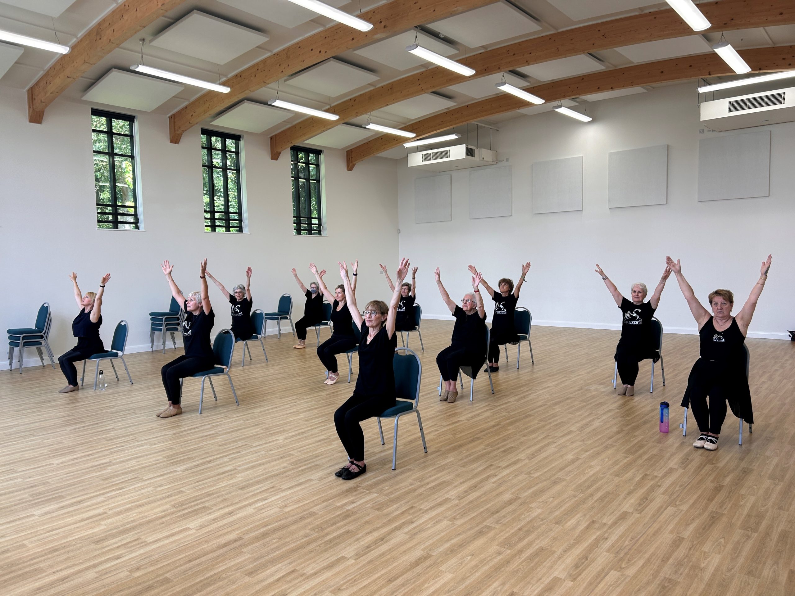 A group of women sitting on chairs in a large room, with their hands in the air.