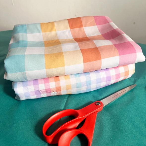 A folded pile of rainbow plaid fabric with a pair of scissors laying in front of it.