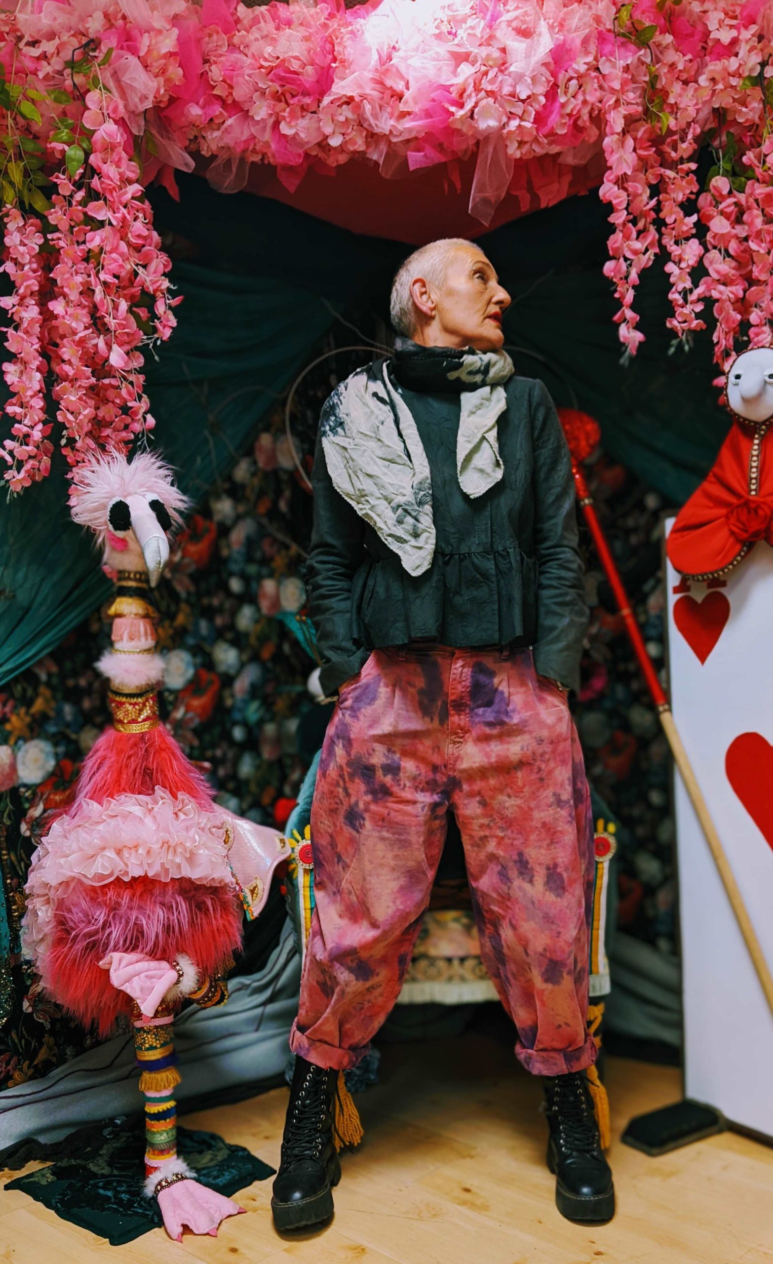 An older white women dressed stylishly, in front of a pink flower background.